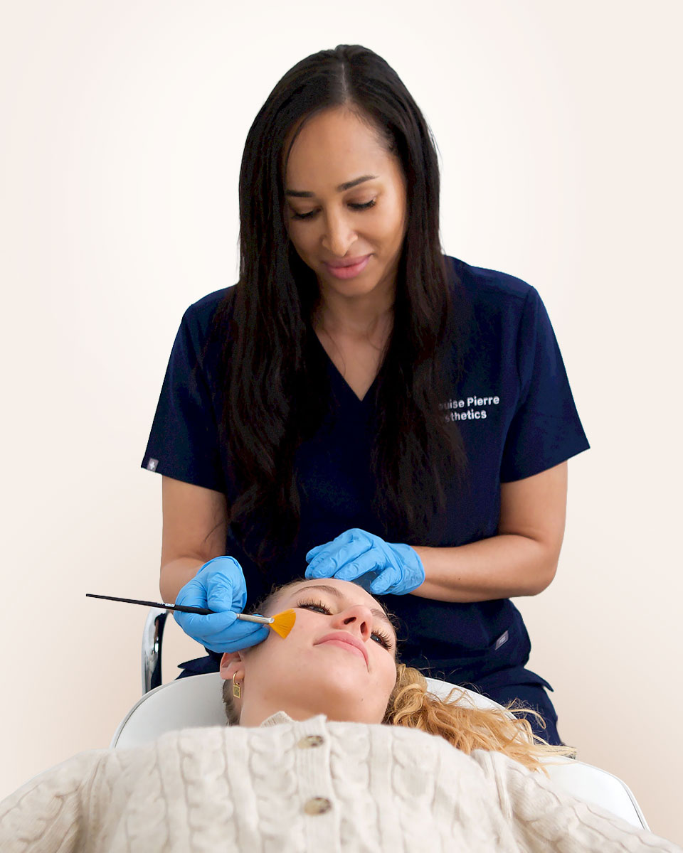 Dr-Louise-Pierre-Client-Treatment Practitioner applying a facial treatment to a client in a clinic setting.