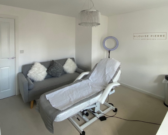 Peacehaven clinic treatment room with adjustable treatment bed, grey sofa with cushions, ring light, and soft neutral décor creating a calm, clean environment.