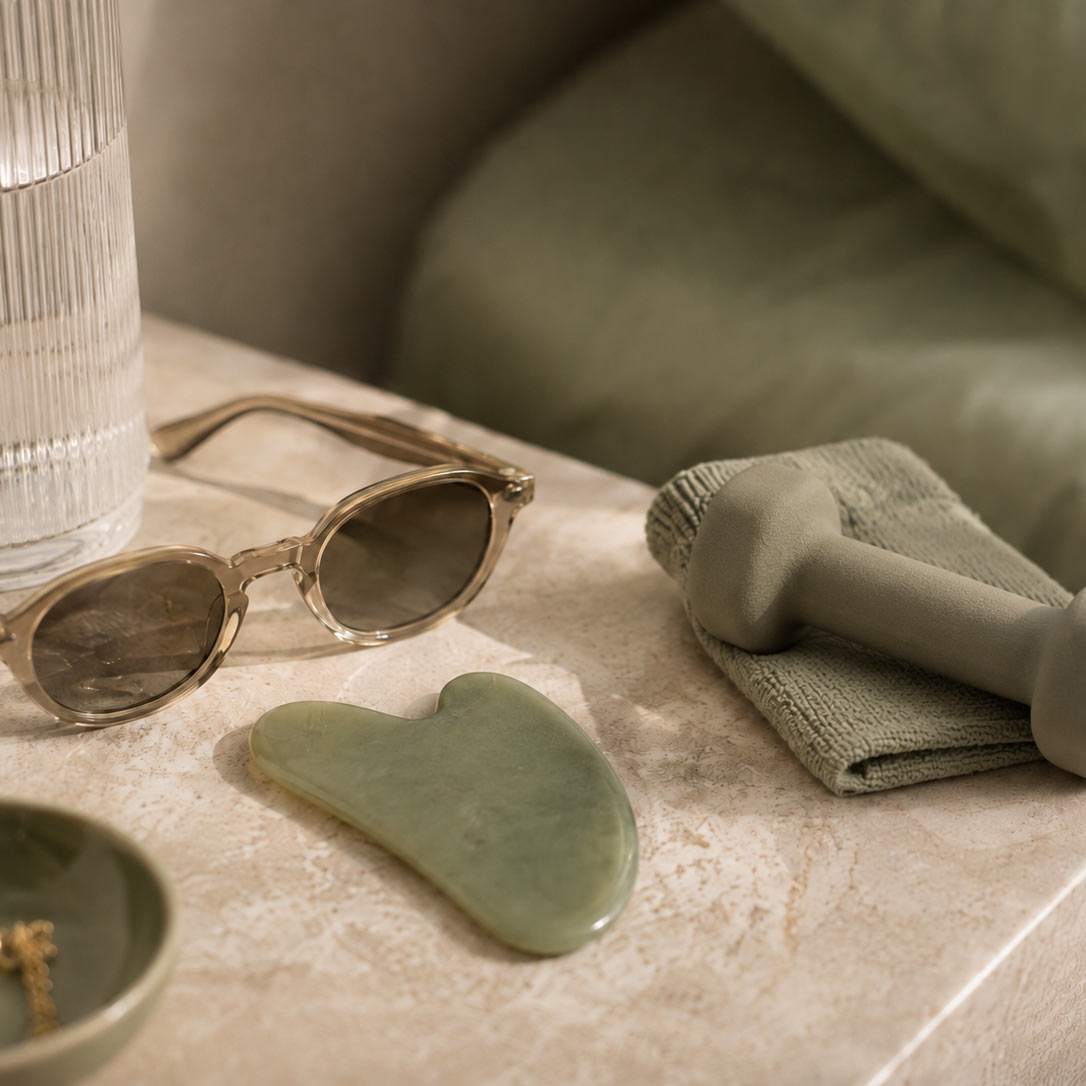 Sunglasses, a gua sha tool and a small dumbbell on a bedside table, representing things to avoid shortly after dermal filler treatment.